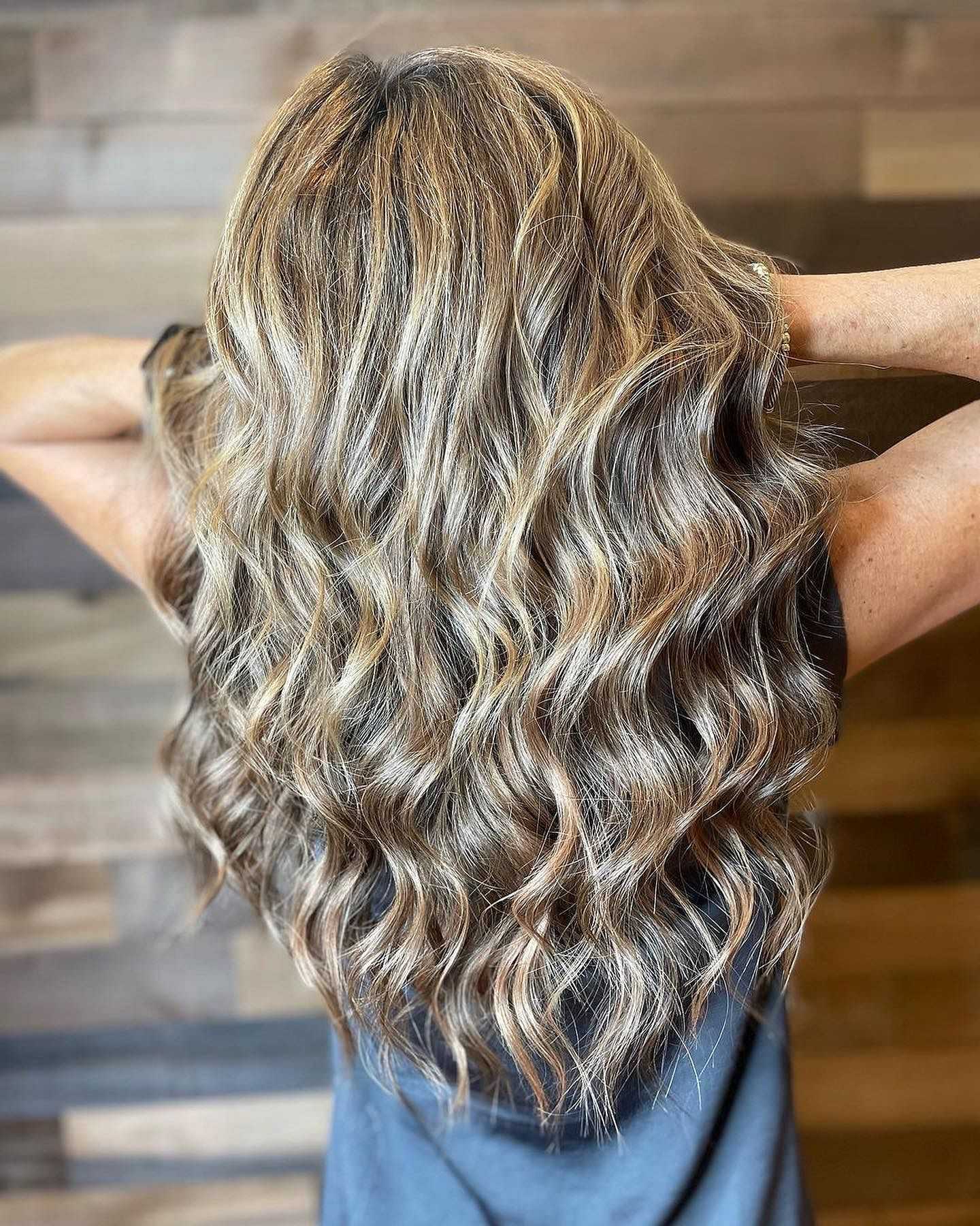 Woman with long, wavy blonde hair and dark roots against a wooden background.